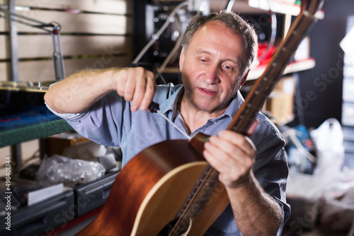 Adult serious male is repairing music instruments in music store.
