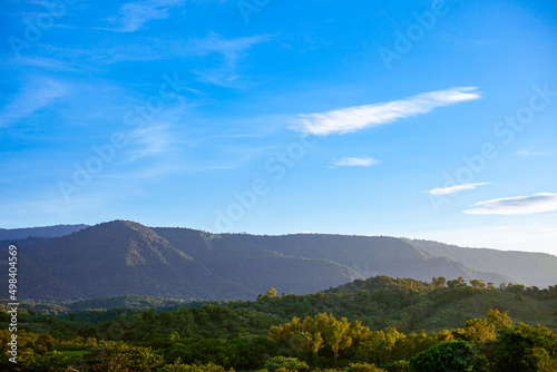 Mountains, flowers, grass and blue sky with white clouds. Background image for design. The concept of nature is bright.