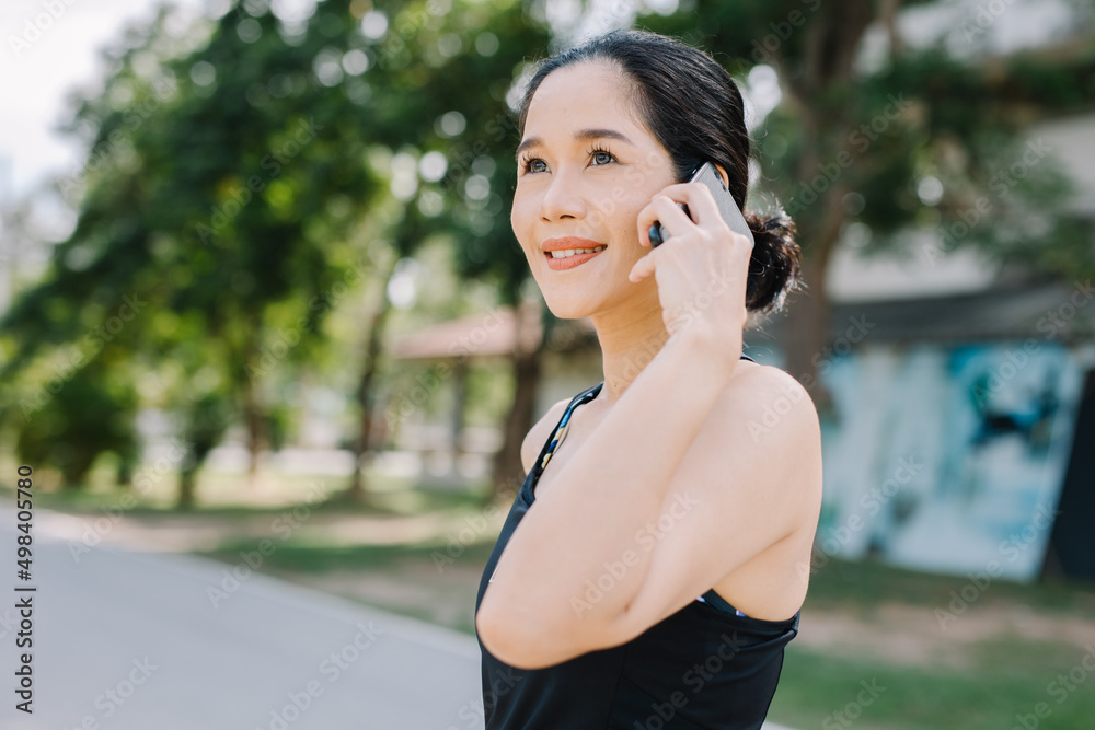 A beautiful woman in the gym stands with a smartphone smiling and looks at the screen outside the building during the day. communication concept