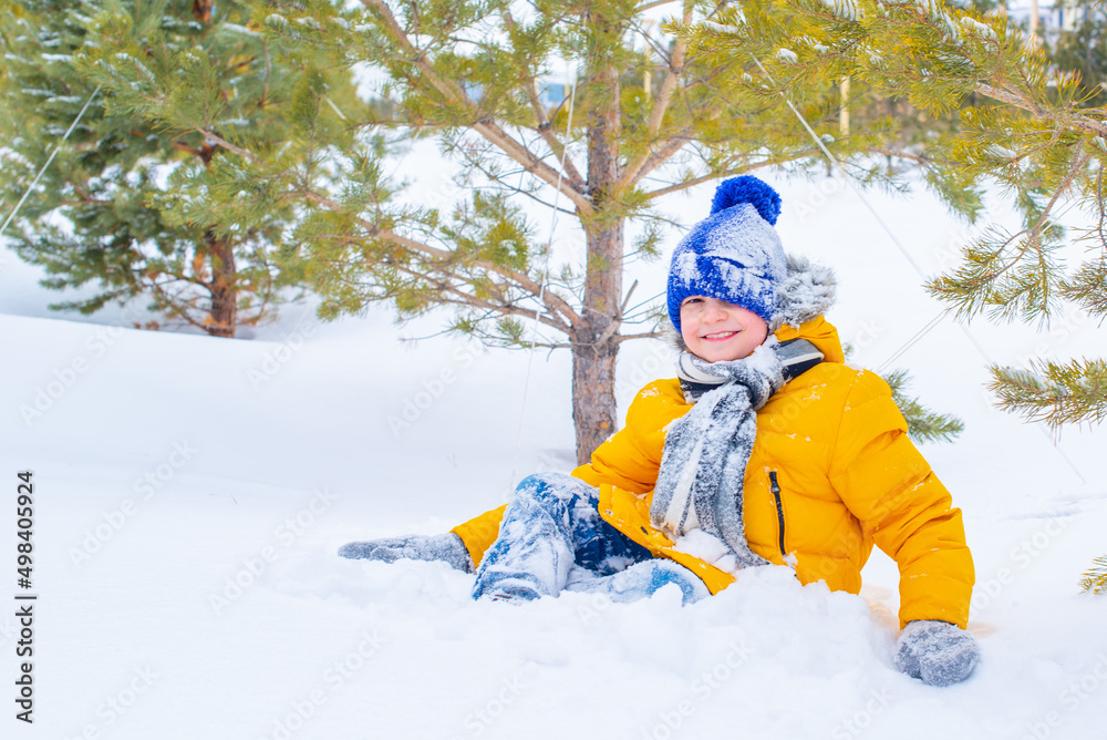 cheerful boy playing snowballs in a yellow jacket and a blue hat