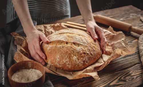 The baker's hands holding homemade natural bread with a Golden crust on a napkin on old wooden background. Rustic style.