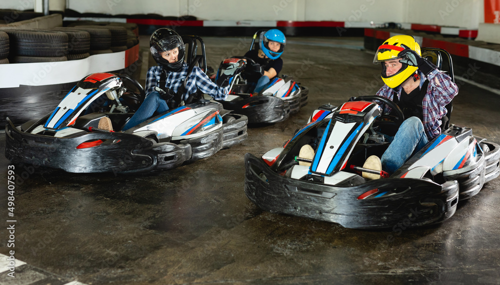 Group of cheerful positive smiling people driving go-carts at racing track