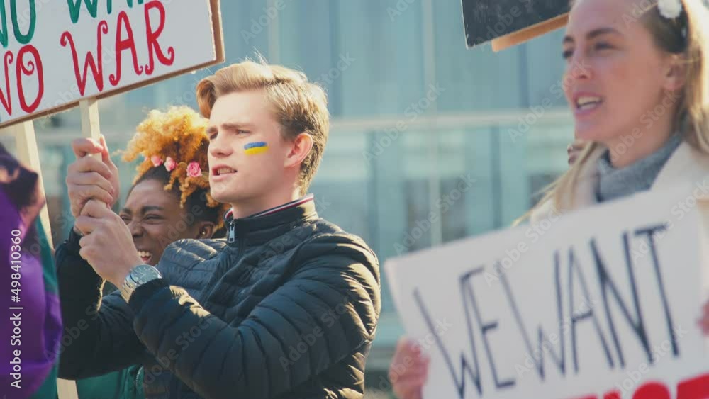 Close up of protestors with Ukranian flag painted on faces holding placards and chanting slogans on demonstration march in city - shot in slow motion
