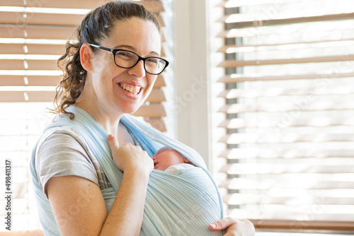 Happy young mother holding her sleeping newborn baby in a wrap sling photo