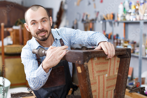 Portrait of furniture restorer inspecting antique armchair for restoration in workshop
