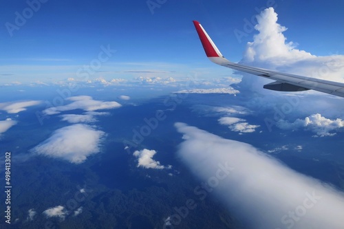 Aerial view of blue sky, white cloud, and green land, view from the window of the plane. Transportation and nature concept.