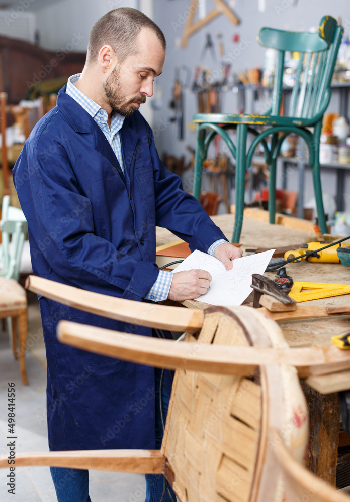 Craftsman making drawing of vintage chair on paper in woodwork studio