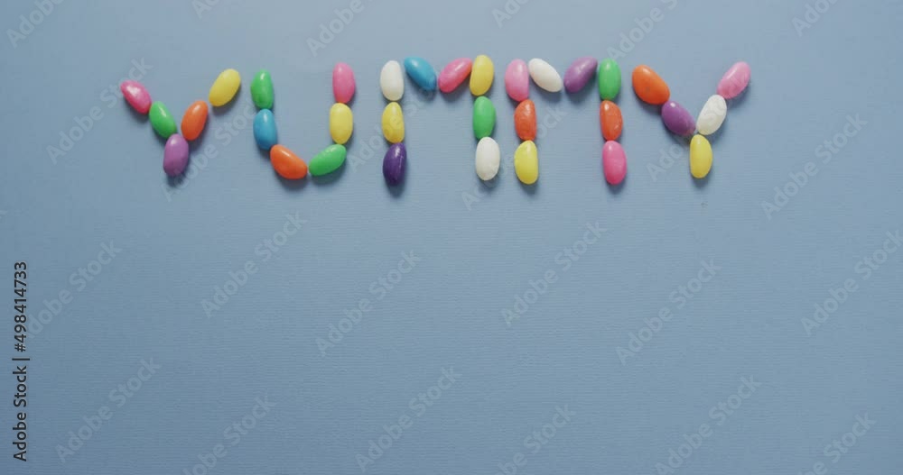 Video of overhead view of yummy text formed multi coloured sweets with copy space on blue background Video of overhead view of yummy text formed multi coloured sweets with copy space on blue background