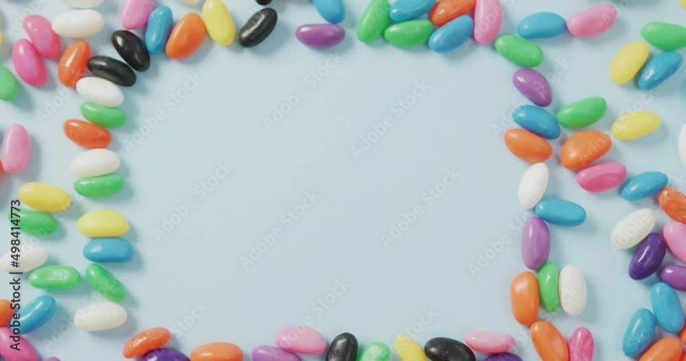Video of overhead view of multi coloured sweets with copy space over blue background