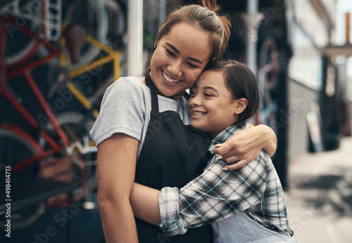 We are actually family. Shot of two young female colleagues sharing a hug outside a bicycle repair shop.