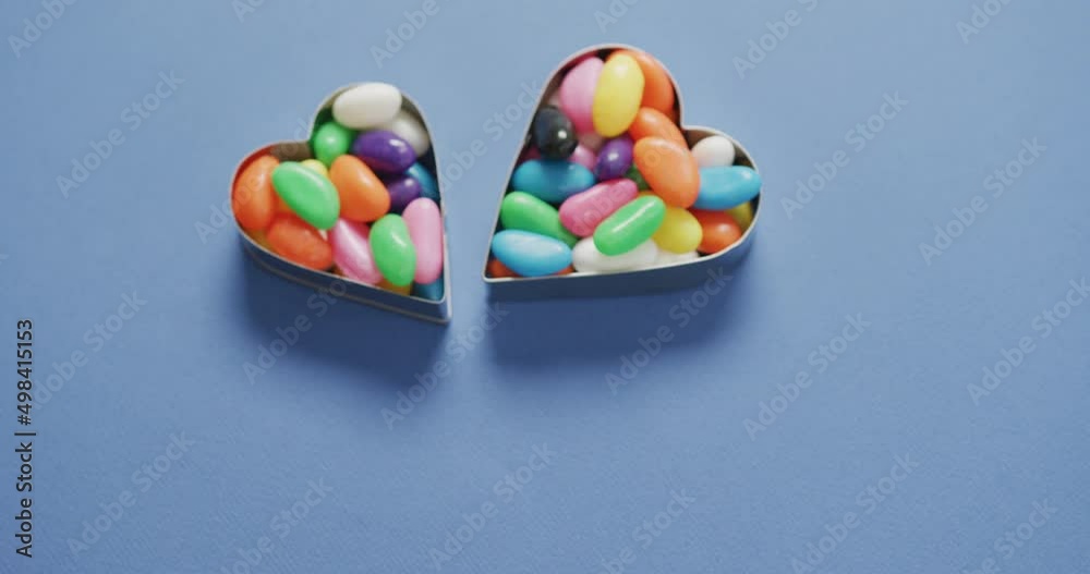 Video of overhead view of multi coloured sweets in two heart shapes over blue background Video of overhead view of multi coloured sweets in two heart shapes over blue background