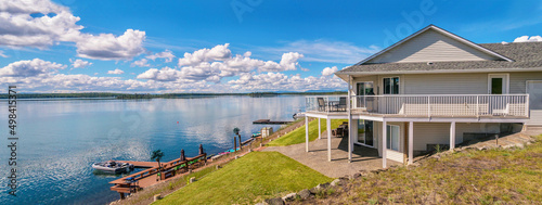 Photo Panoramic view of a beautiful, large modern luxury summer holiday home, featuring sun decks, glass railings, and large windows, set beside a small lake in central British Columbia, Canada