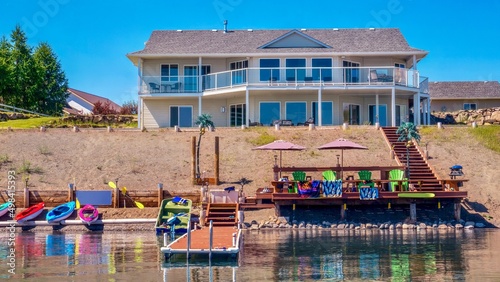 A beautiful contemporary two-story beach house, with large windows, wraparound deck and glass railings, waterfront recreation area, and boat dock. British Columbia, Canada.
