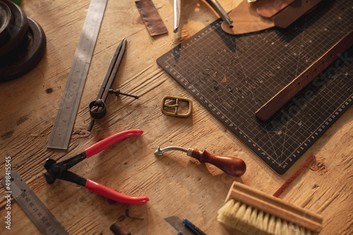 High angle view of various leather tools with cutting mat on wooden table in workshop photo