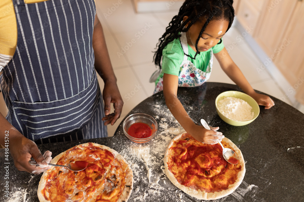 African american girl spreading sauce on pizza bread by father standing at kitchen counter African american girl spreading sauce on pizza bread by father standing at kitchen counter