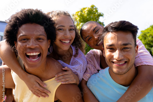 Portrait of smiling multiracial men giving piggyback rides to women on sunny day photo