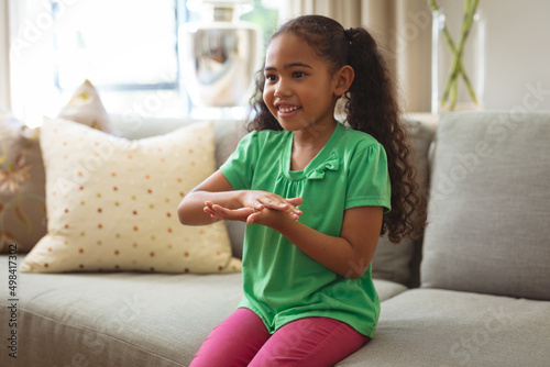 Smiling multiracial mute girl talking through hand sign language sitting on sofa at home