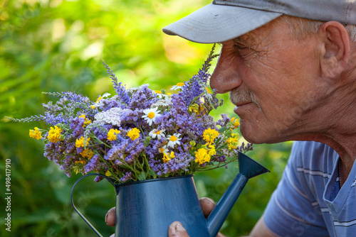 Old man smelling wild flowers in a blue metal watering can in his backyard