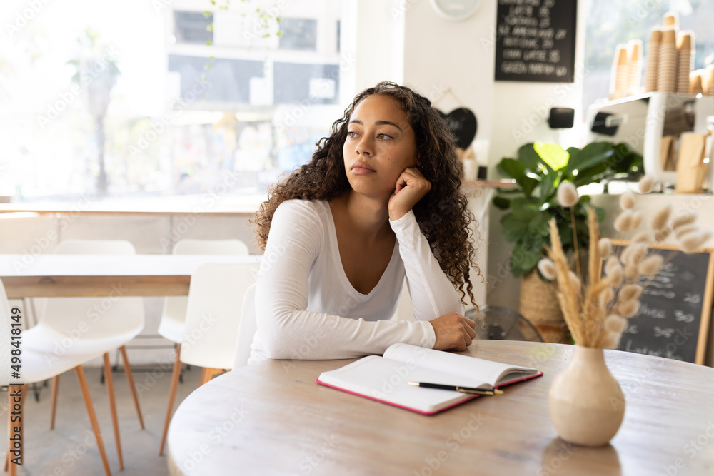 Bored young african american woman leaning on hand while sitting with diary at table in cafe Bored young african american woman leaning on hand while sitting with diary at table in cafe