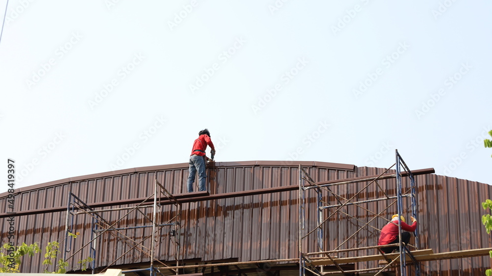 Male workers are roofing the dome. Workers cover with metal sheet of metal scaffolding in the bottom view on a sky background. Selective focus