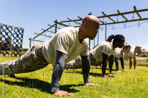 Group of male and female diverse soldiers performing push ups together at boot camp photo