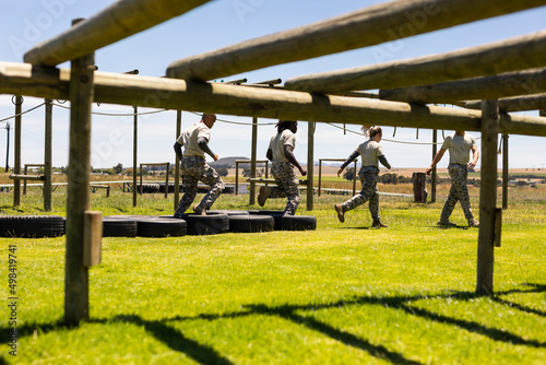Group of diverse male and female soldiers walking on tires during obstacle course at boot camp photo