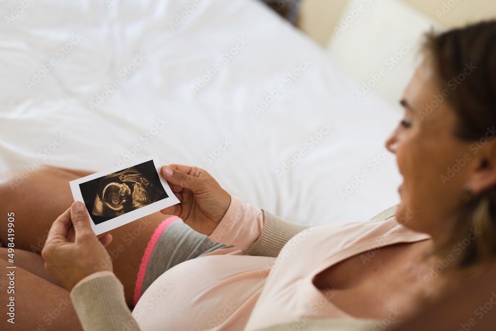 Caucasian pregnant woman smiling while holding ultrasound image of her baby at home Caucasian pregnant woman smiling while holding ultrasound image of her baby at home