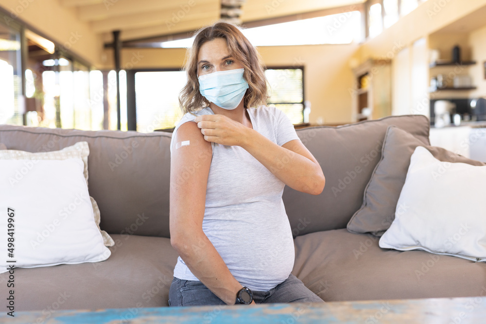 Caucasian pregnant woman wearing a face mask showing her shoulder after getting the vaccine Caucasian pregnant woman wearing a face mask showing her shoulder after getting the vaccine
