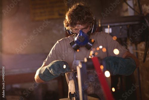 Blacksmith wearing gas mask while working on metal in manufacturing industry photo