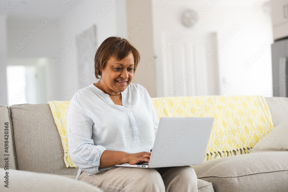 Smiling african american senior woman using laptop while sitting on sofa at home Smiling african american senior woman using laptop while sitting on sofa at home