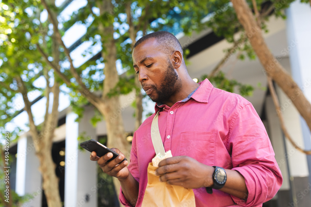 African american businessman having a snack and using smartphone while on the go to office African american businessman having a snack and using smartphone while on the go to office