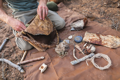 Midsection of young male caucasian survivalist with handmade leather bag kneeling by various objects photo