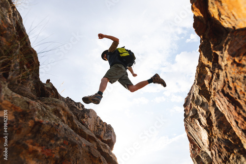 Low angle view of energetic male caucasian adventurer in mid-air while jumping from rocky cliff photo