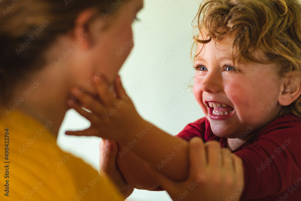 Smiling blond boy playing while touching mother's cheek in kitchen at home Smiling blond boy playing while touching mother's cheek in kitchen at home