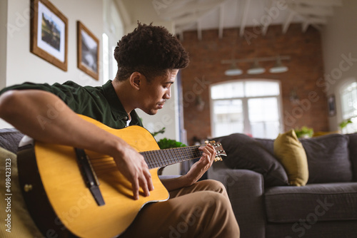 Young biracial man practicing acoustic guitar in living room at home photo