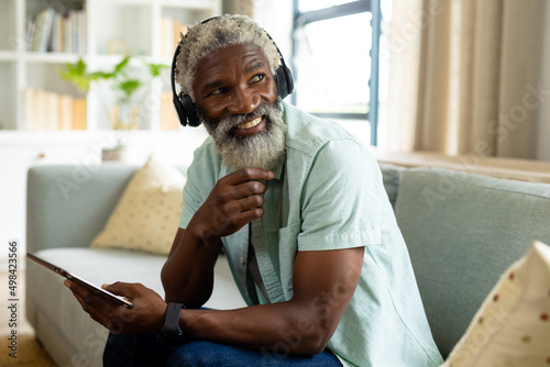 Smiling african american man listening music through headphones while sitting with digital tablet photo