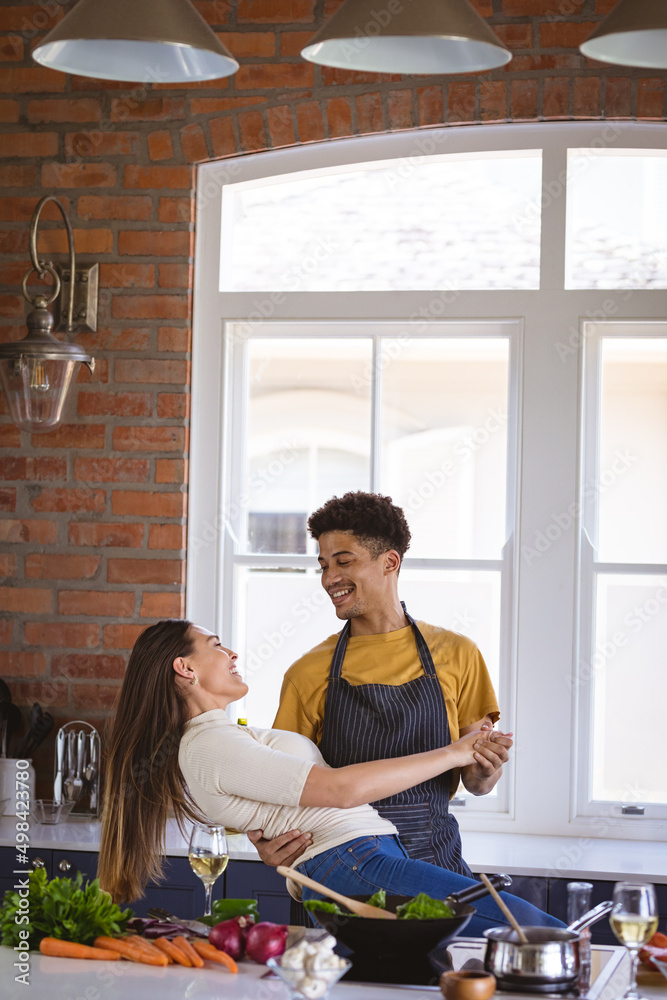 Happy biracial young couple enjoying a dance while preparing meal in kitchen Happy biracial young couple enjoying a dance while preparing meal in kitchen