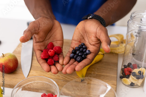 Hands of african american man holding fresh raspberries and blueberries in kitchen at home photo