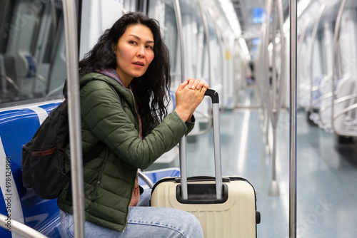 Asian woman with suitcase sitting in subway car