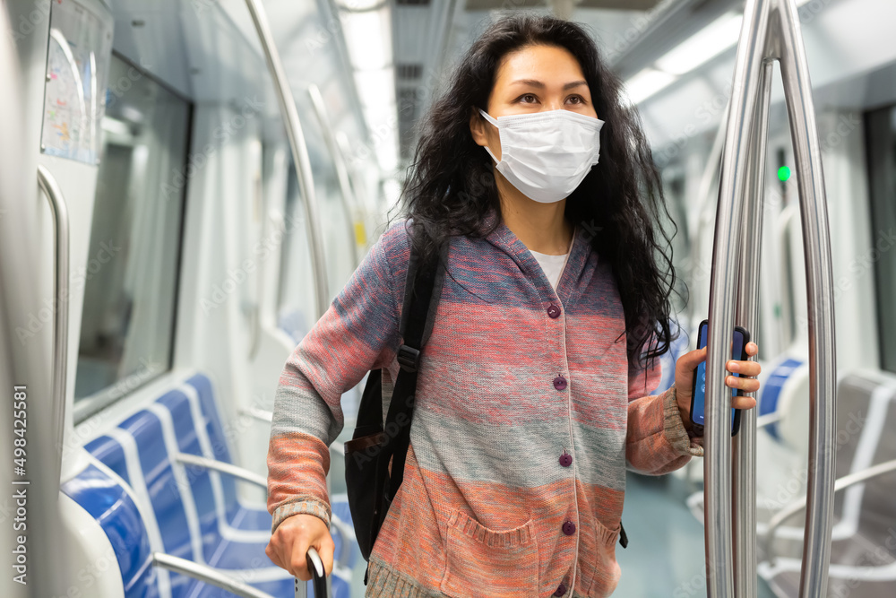 Obraz premium Positive woman passenger in face mask for disease protection standing in subway car, using public transport in big city