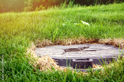 Broken manhole cover. Cracked metal in the grass. Selective focus