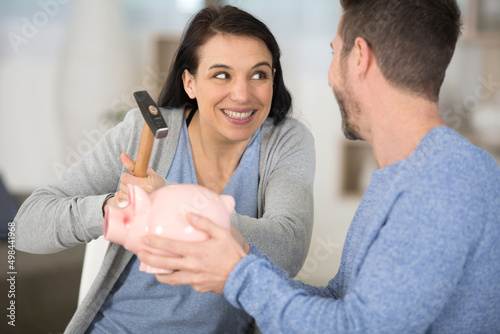 young couple breaking piggy bank with hammer at home