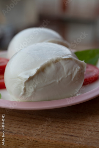 White ball of Italian soft cheese Mozzarella di Bufala Campana with fresh green basil and red tomato