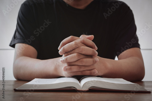 Fotobehang Praying hands placed on a bible on a wooden table against a white room background