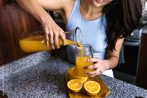 Bild auf Leinwand Hispanic brunette young latin woman preparing orange juice at the kitchen in Mex