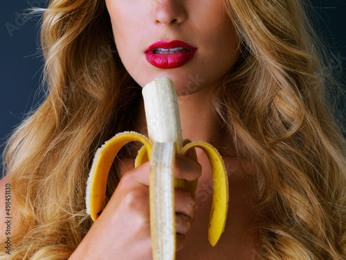 Because who doesnt like a tasty banana now and then. Cropped studio shot of a young woman eating a banana suggestively against a dark background. photo