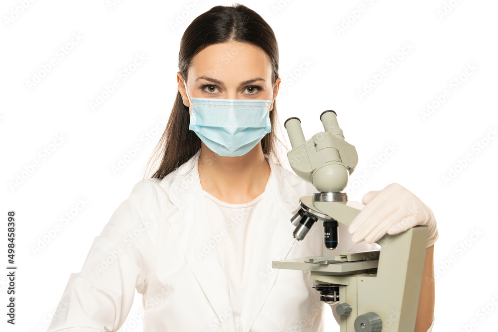 Portrait of smiling female scientist with microscope and face mask on a white background
