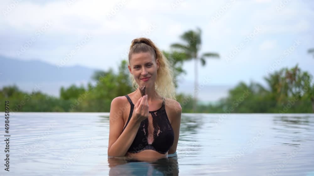 Beautiful Caucasian Woman Tourist Smiling At The Camera Eating Ice Cream In Tropical Swimming Pool - Medium Shot Beautiful Caucasian Woman Tourist Smiling At The Camera Eating Ice Cream In Tropical Swimming Pool - Medium Shot