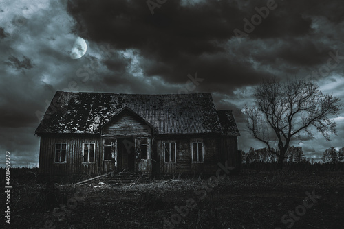 Old wooden house,dramatic clouds at night. Abandoned Haunted Horror House.Near is one tree at night with a moon.
