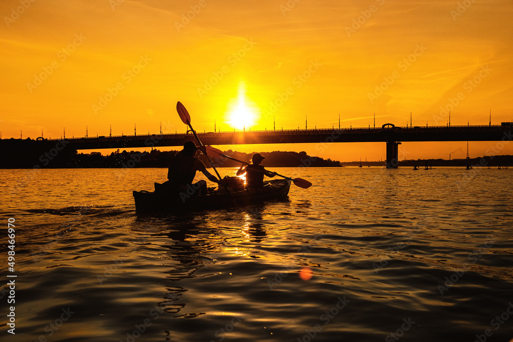 Silhouettes of people in kayak at sunset. Young married couple is boating on river.